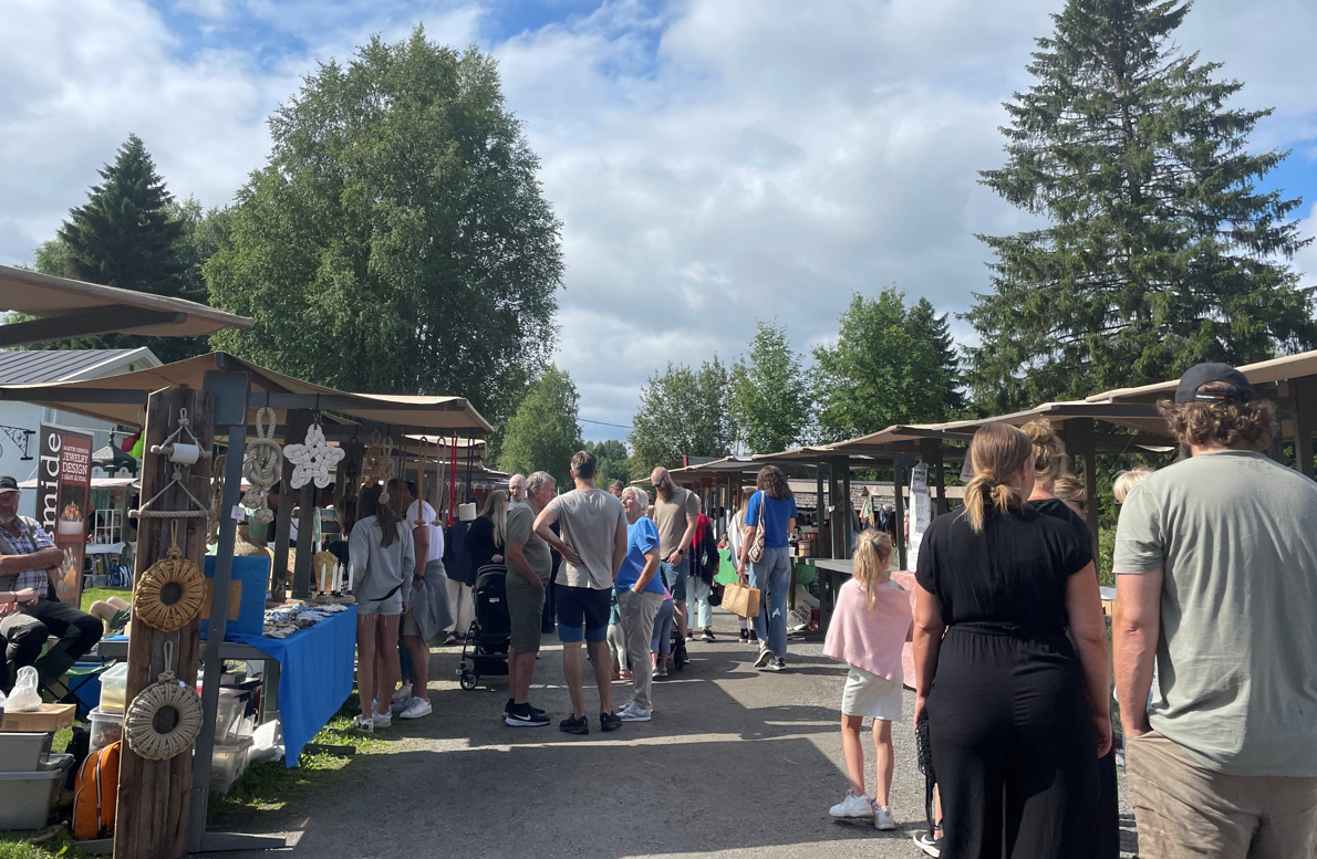 Två rader med marknadsstånd på en grusväg där människor strosar runt
